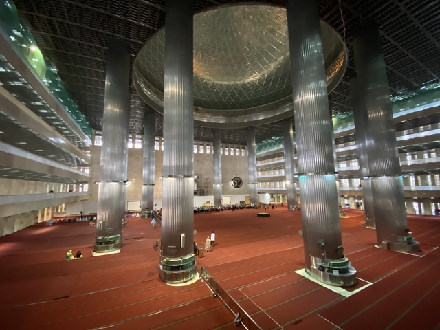       Interior of a large, modern mosque with tall pillars.
  