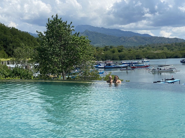       Two women in a pool with a scenic view of boats and mountains.
  