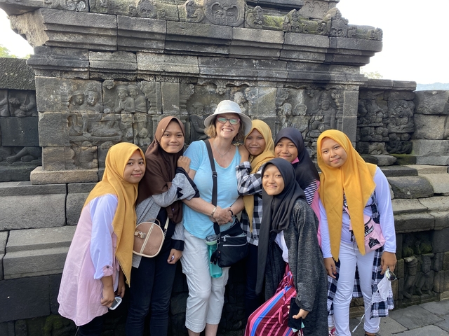       Woman with local girls in front of a stone carving wall.
  