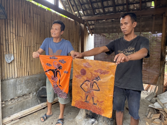       Two men showing traditional textile art.
  