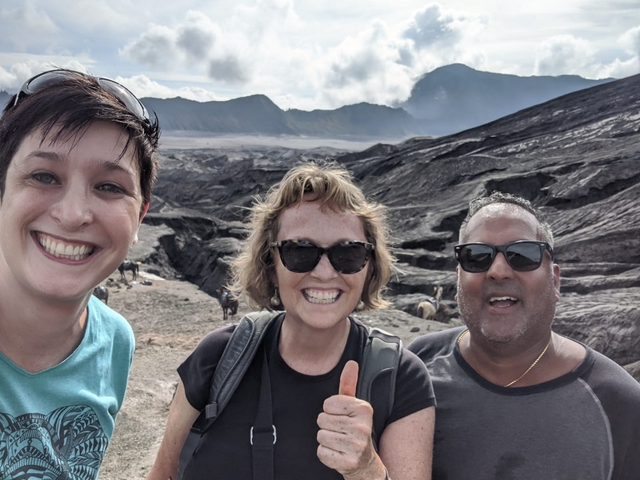       Three smiling people with a volcanic landscape in the background.
  