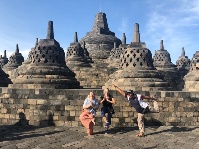       Three people posing in front of an ancient temple with stupa structures.
  