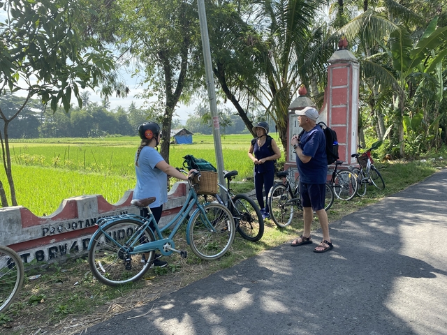       People with bicycles along a rural road surrounded by fields.
  