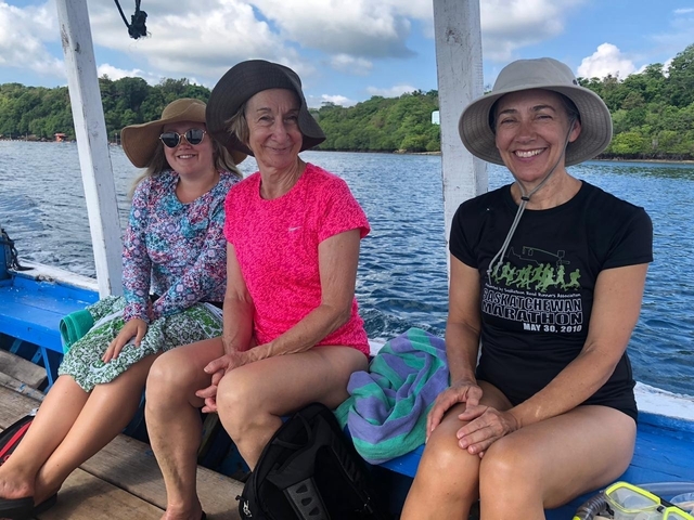       Three women on a boat surrounded by water and greenery.
  
