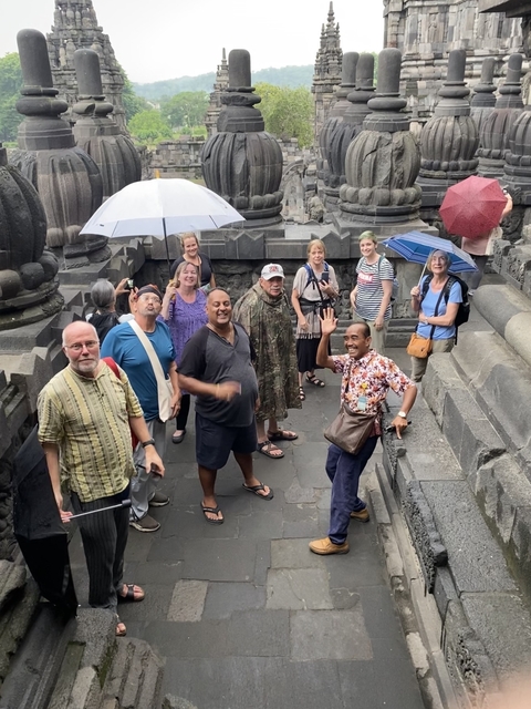       Group of people with umbrellas exploring a historic site.
  