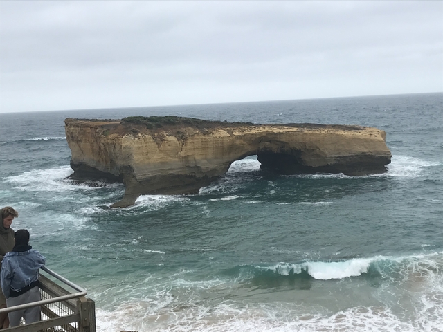 A rock formation in the ocean with people observing.