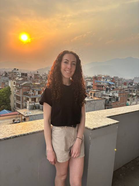       Person posing on a rooftop with a sunset background.
  