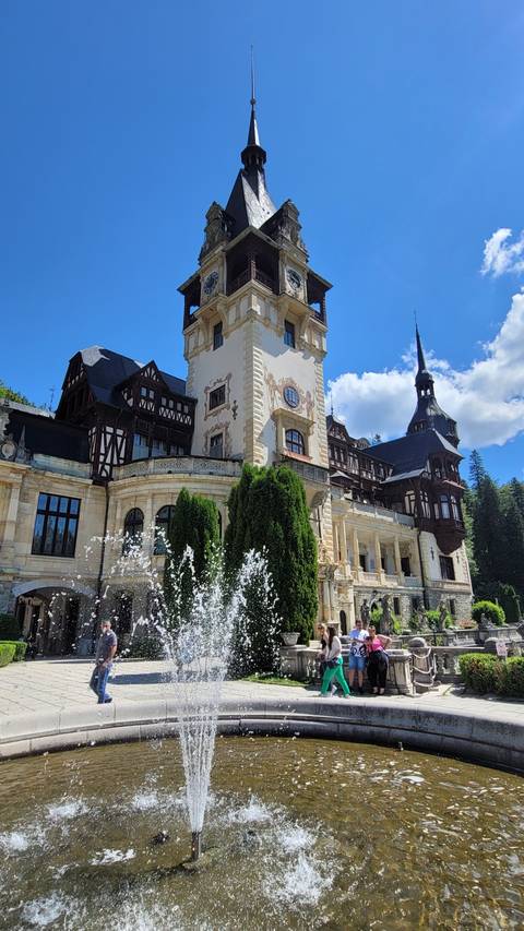 A historic castle with a fountain and tourists around.