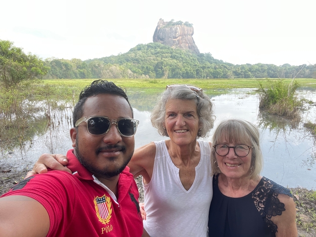 Three people posing in front of a large rock formation and lake