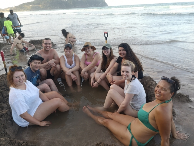       Group of people in a sandy hot spring pool by the sea.
  