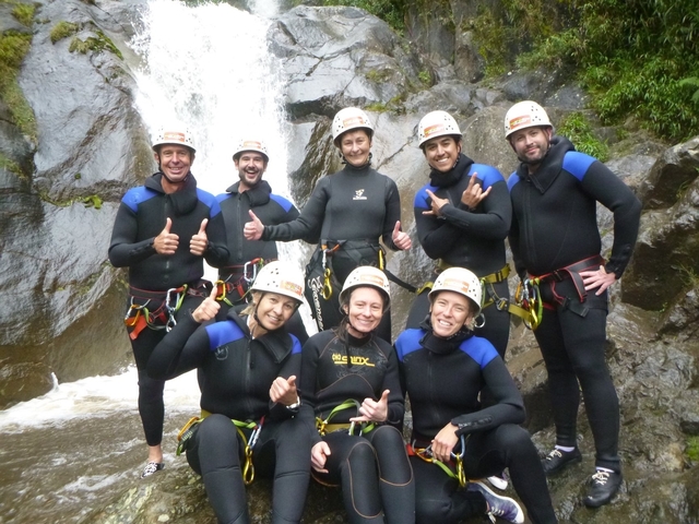      Group of people in wetsuits and helmets posing in front of a waterfall.
  