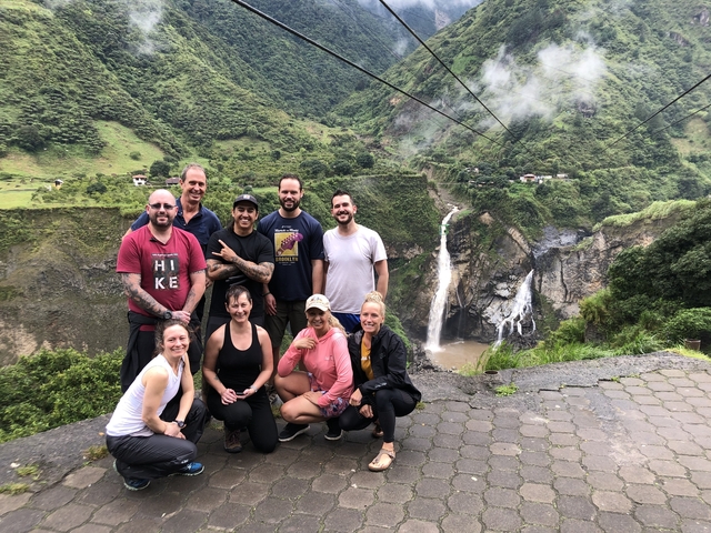       Group of people posing with a distant waterfall in a green valley.
  