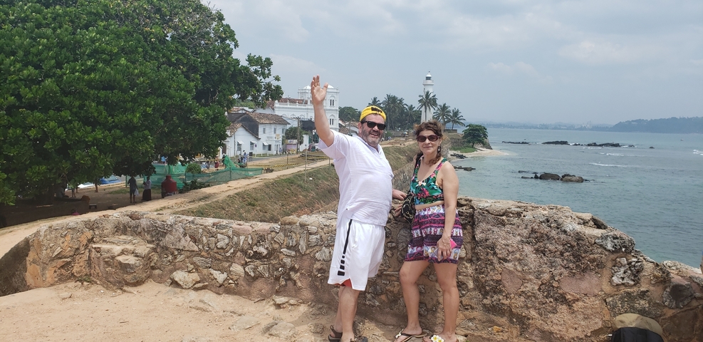       Couple posing at a fort with a lighthouse in the background.
  