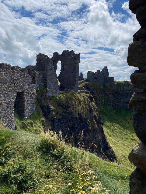 Historic stone ruins on green cliffs under a blue sky.