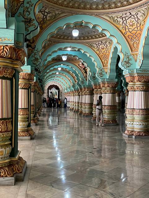 People walking inside a grand, ornately decorated hallway.