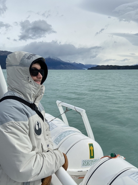       Person in winter clothing on a boat with mountains in background.
  