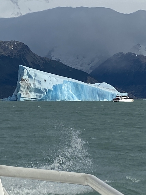 Large iceberg floating in the ocean with a boat nearby.