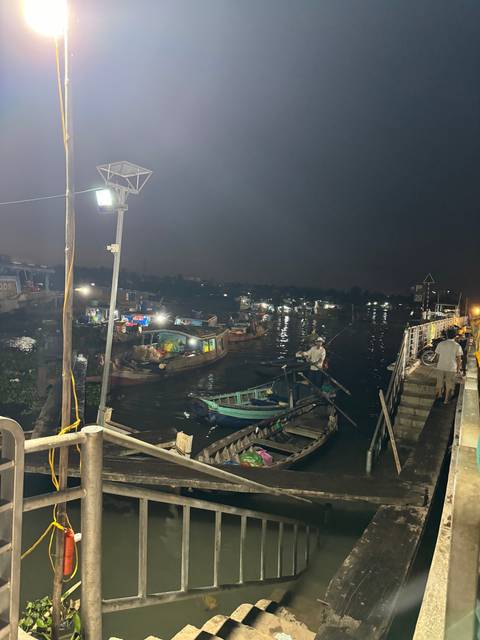 Boats on a river at night with lights reflecting on water.