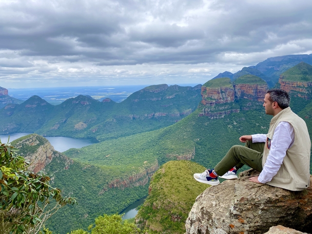       Person sitting on a cliff edge overlooking a mountainous valley.
  