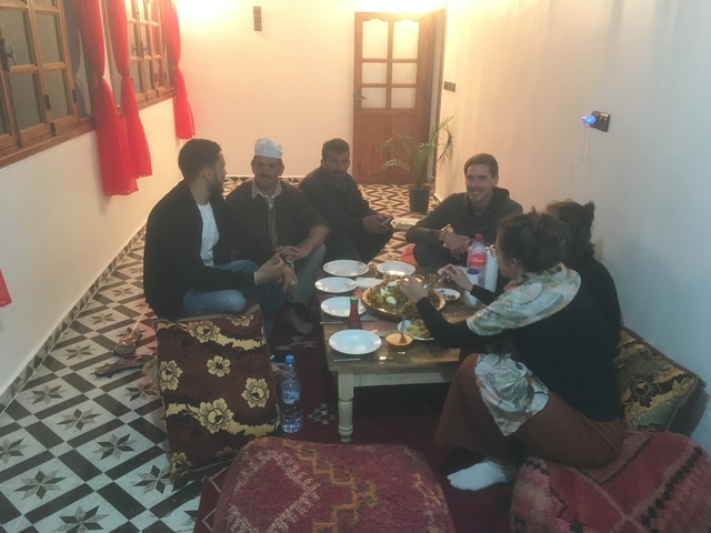 Group of people sitting on floor having a meal together.