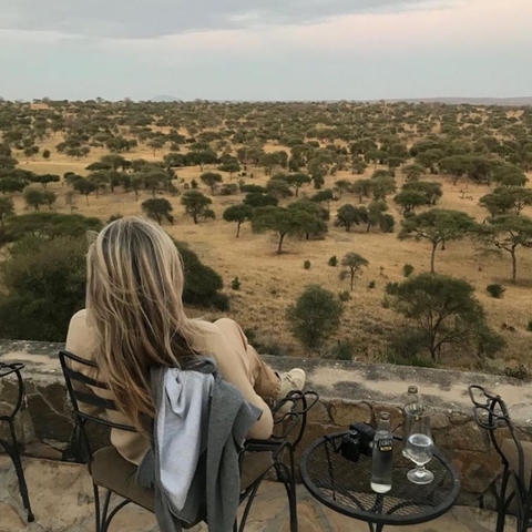 Person sitting on a terrace overlooking a scenic savannah landscape with trees.