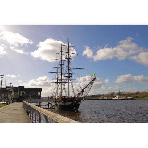 Historic ship docked at a waterfront with flags flying.