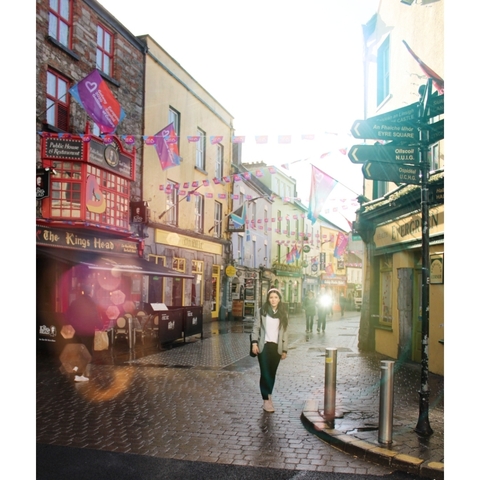 Person standing in a vibrant street with shops and flags.