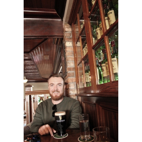 Person sitting in a pub with bottles visible in a cabinet.