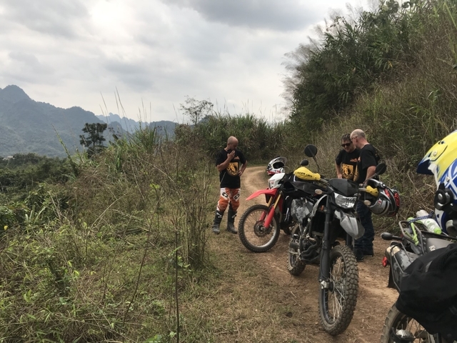 Motorcyclists discussing by their bikes on a dirt road with mountains in the distance.