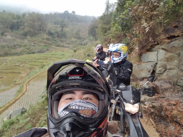 Four people in motorcycle gear with a view of terraced fields.