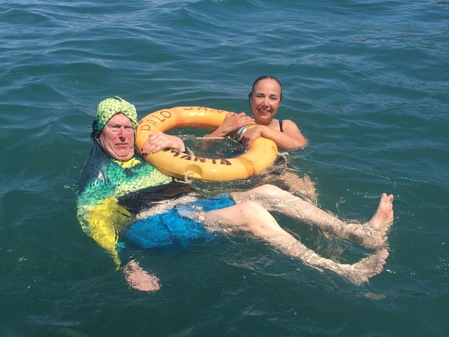       Two people swimming in the ocean, one in a costume holding a flotation device.
  