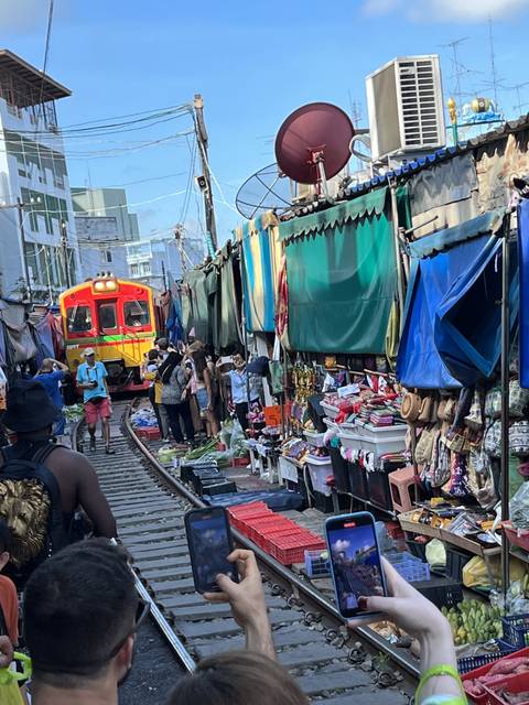       A busy market with a train passing through and people taking photos.
  