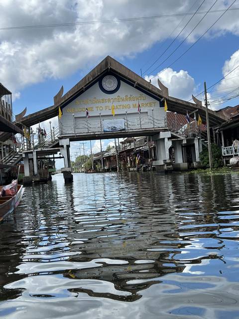       An entrance sign to a floating market with water in the foreground.
  