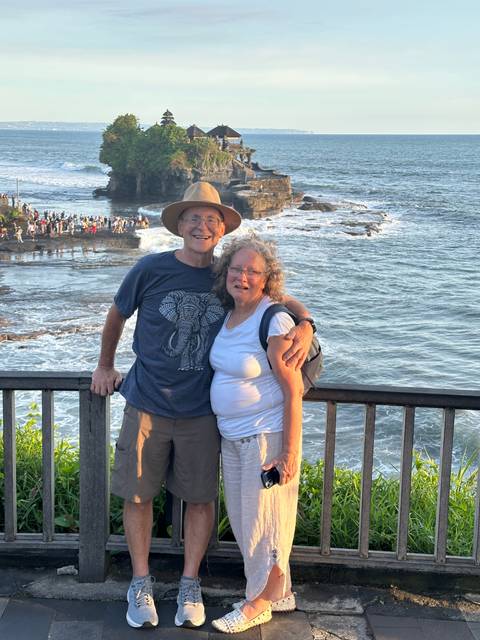 Couple standing by the ocean with rock formations in the background.