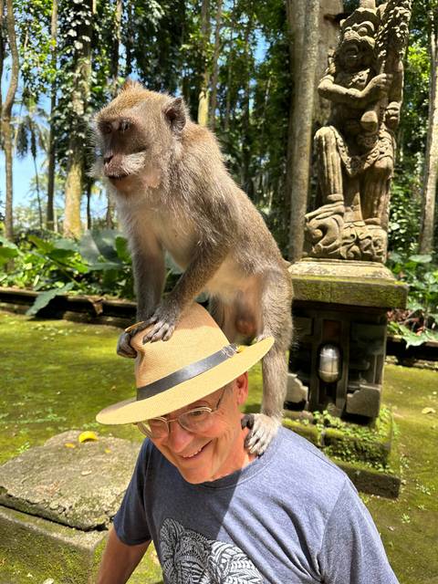       A person with a monkey on their shoulder in a tropical setting.
  
