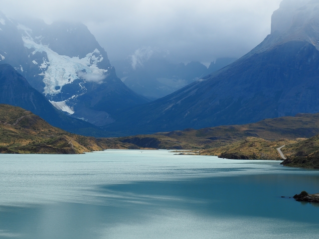       A calm lake with mountains and low clouds in the background.
  