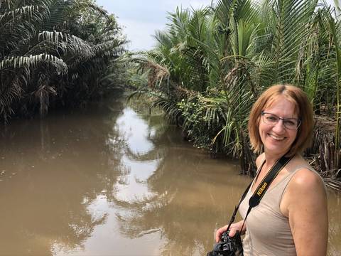       Woman standing beside a river with lush greenery.
  