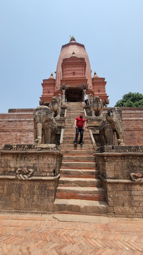       Person descending steps lined with sculptures at a temple site.
  