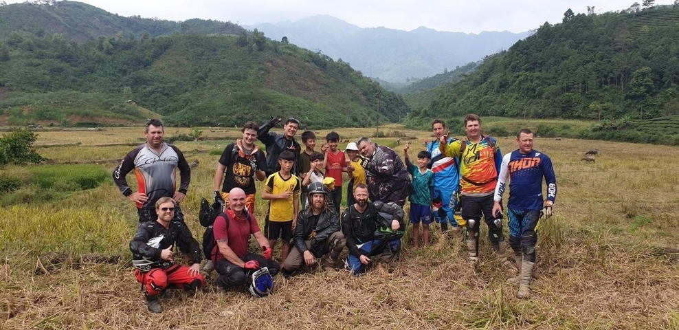 Group of motorcyclists posing with children in a field.