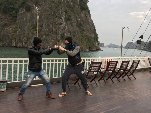 Two people play fighting on a boat deck with limestone cliffs in the background.