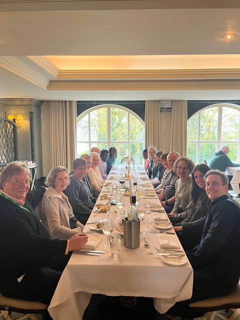       A group of people sitting at a long dining table inside a room.
  