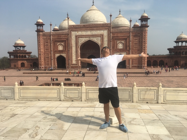       Traveller with arms outstretched joyfully faces the red sandstone mosque beside the Taj Mahal complex
  