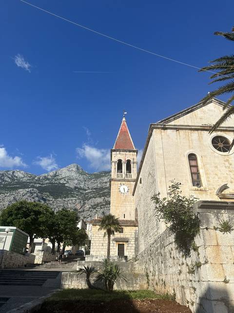 A stone church tower with a mountain backdrop under a clear blue sky.