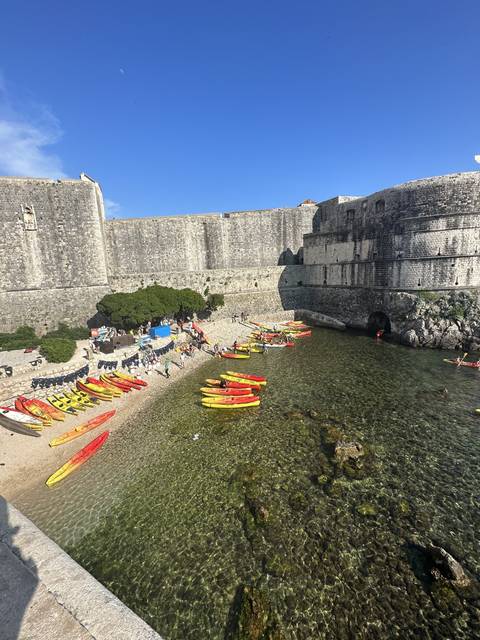 A group of kayakers near stone walls in a sunny coastal area.