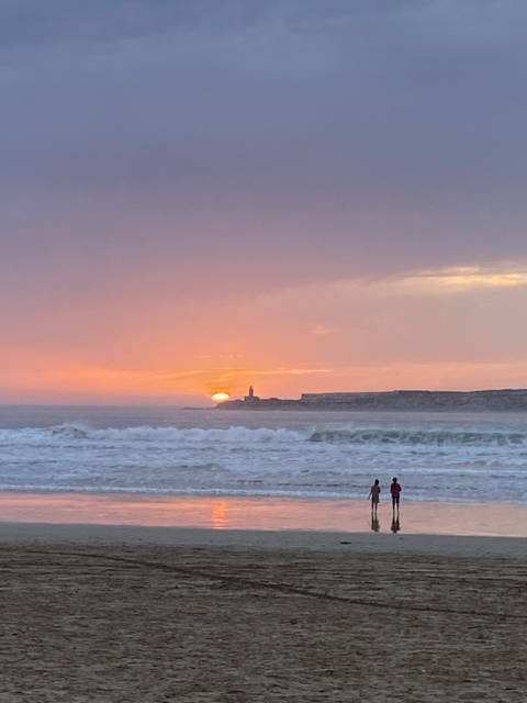 Beach at sunset with two people near water.