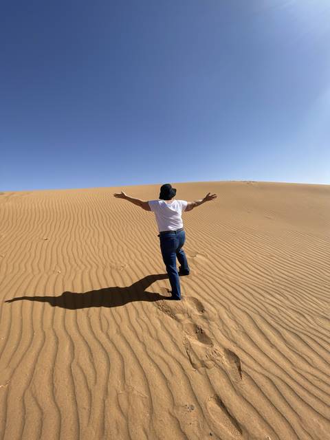 Person posing on a sand dune in a desert.