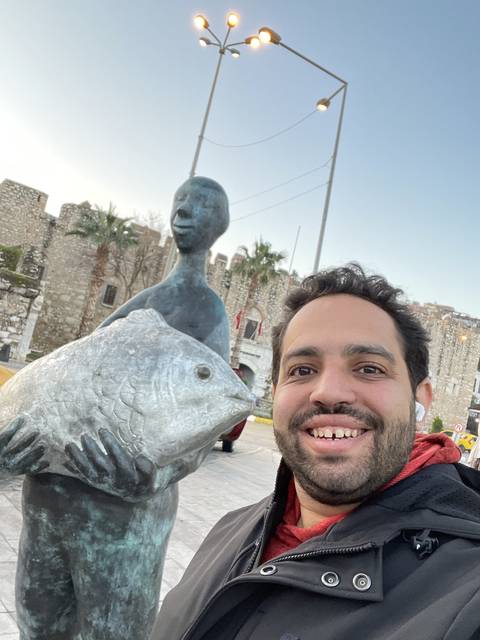 Smiling person taking a selfie with a fish sculpture.