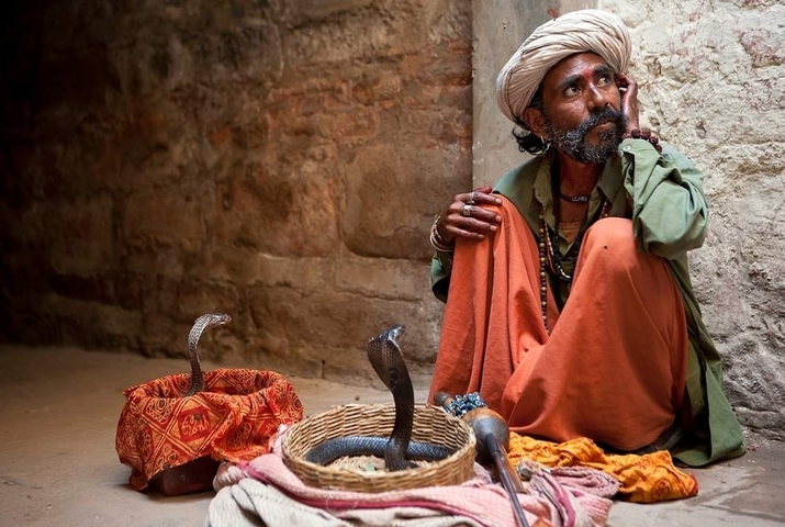 A man seated beside two cobras in baskets within a narrow alley.