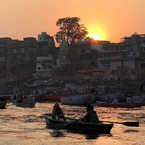 Boats on the Ganges River with a vibrant sunset backdrop of Varanasi cityscape.