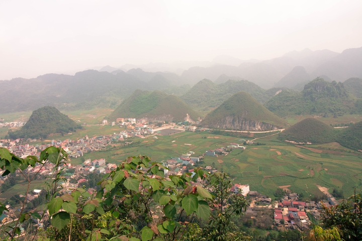       An elevated view of a valley with fields, houses, and conical hills.
  